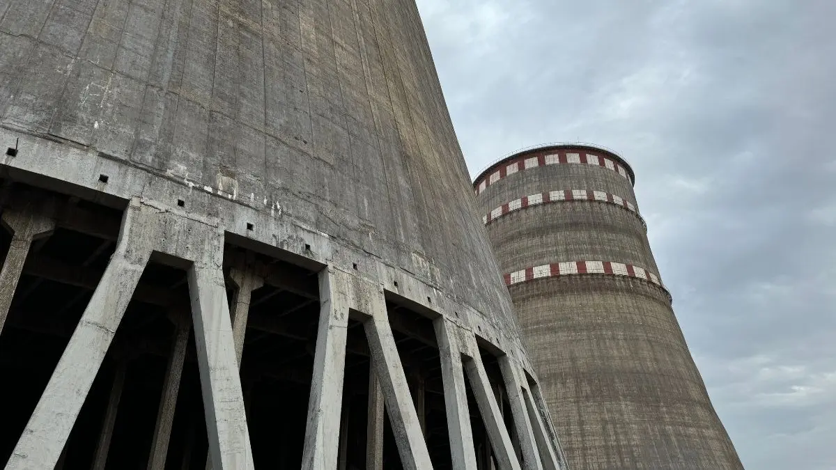 A low-angle view of the massive concrete cooling towers at the Zaporizhzhia Nuclear Power Plant under a cloudy sky.