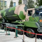 A green and brown camouflaged Chinese DF-31 intercontinental ballistic missile mounted on a heavy transport erector launcher truck, displayed outdoors as part of a military exhibition.