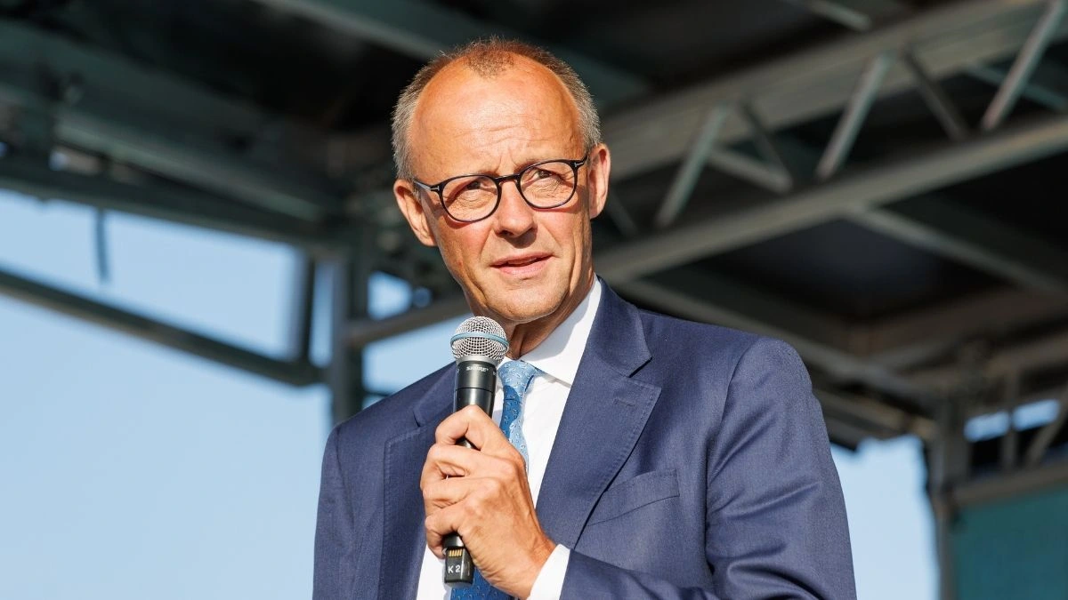 A man in glasses holding a microphone while speaking at an outdoor event