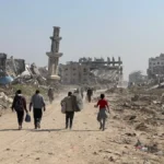 Displaced residents walking through heavy concrete rubble and destroyed infrastructure in the Gaza Strip.