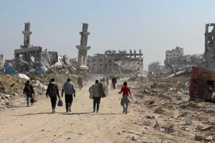 Displaced residents walking through heavy concrete rubble and destroyed infrastructure in the Gaza Strip.