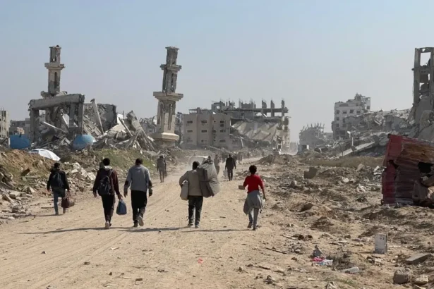 Displaced residents walking through heavy concrete rubble and destroyed infrastructure in the Gaza Strip.