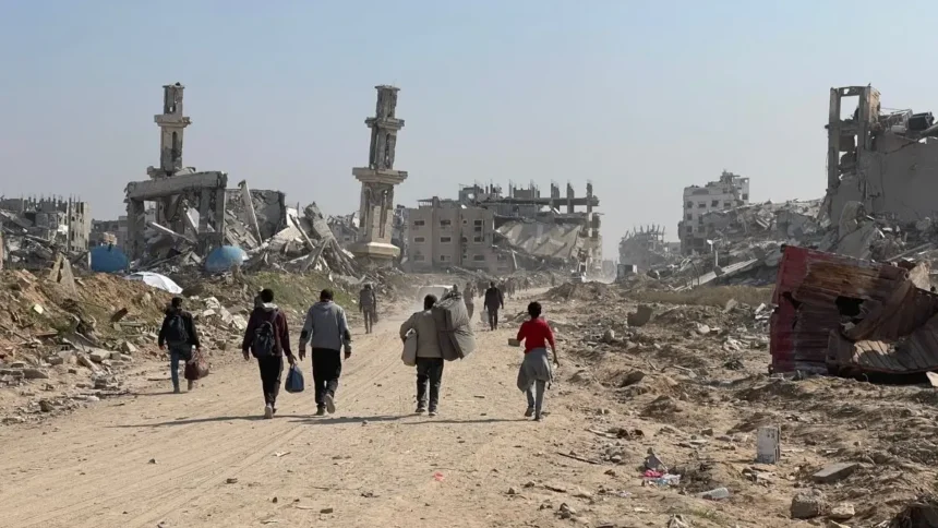 Displaced residents walking through heavy concrete rubble and destroyed infrastructure in the Gaza Strip.