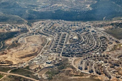 Aerial view of an Israeli settlement in the occupied West Bank, showing dense concrete housing units strategically dividing the surrounding agricultural landscape.