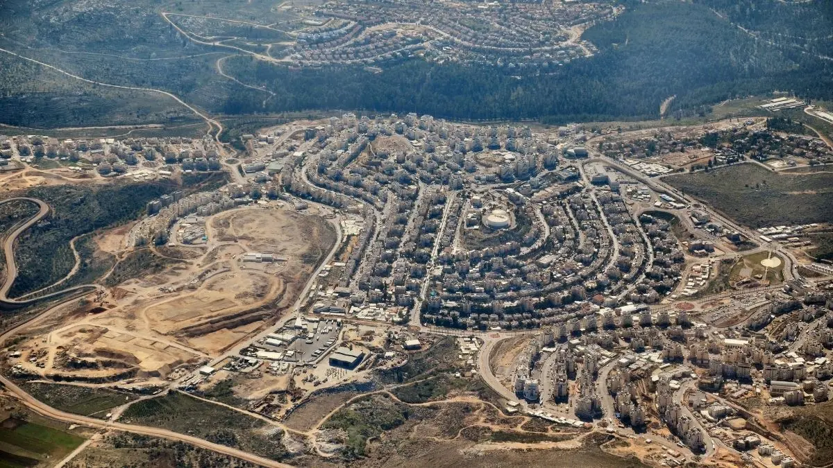 Aerial view of an Israeli settlement in the occupied West Bank, showing dense concrete housing units strategically dividing the surrounding agricultural landscape.