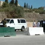 Israeli soldiers stop a Red Crescent ambulance and a van at a concrete-block roadblock checkpoint in the West Bank