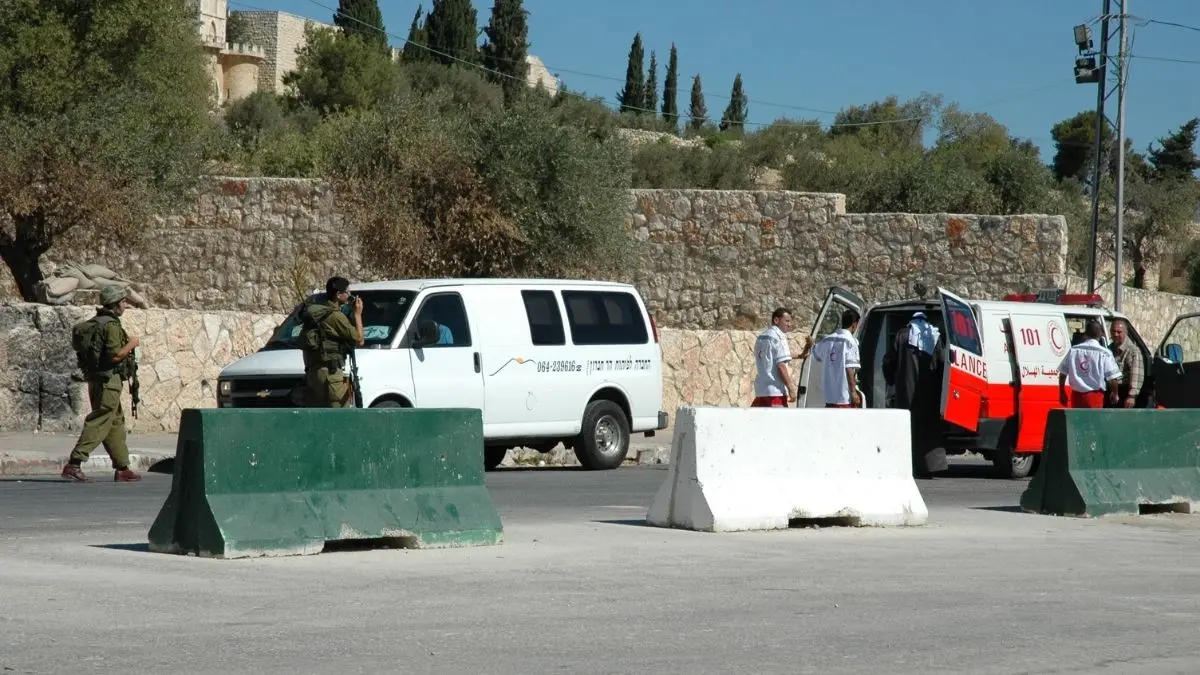 Israeli soldiers stop a Red Crescent ambulance and a van at a concrete-block roadblock checkpoint in the West Bank